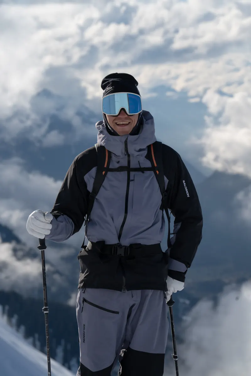 Adrian „Adschi“ Haginger lächelnd mit Ski-Ausrüstung über den Wolken